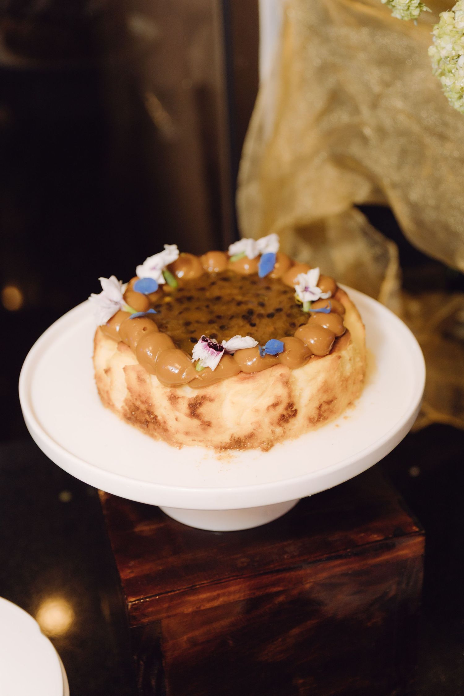 Decorative bundt cake with caramel glaze and edible flowers displayed on a white pedestal cake stand.