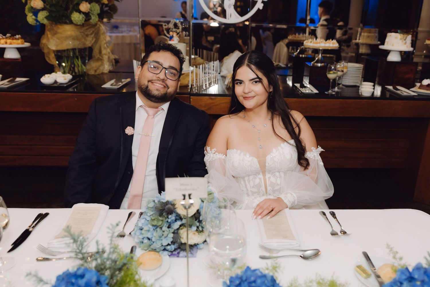 Bride and groom smiling together at their wedding reception table decorated with blue floral centerpieces.