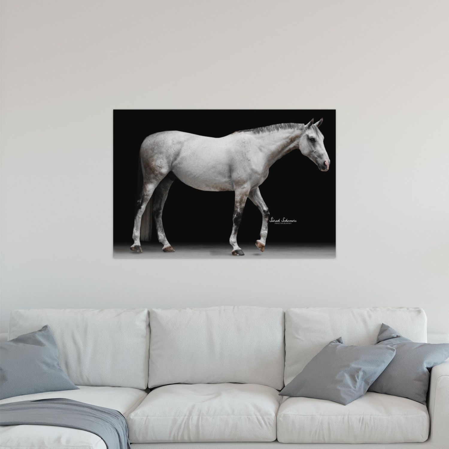 A white horse stands against a dark background in a dramatic wall art print displayed above a modern white sofa.