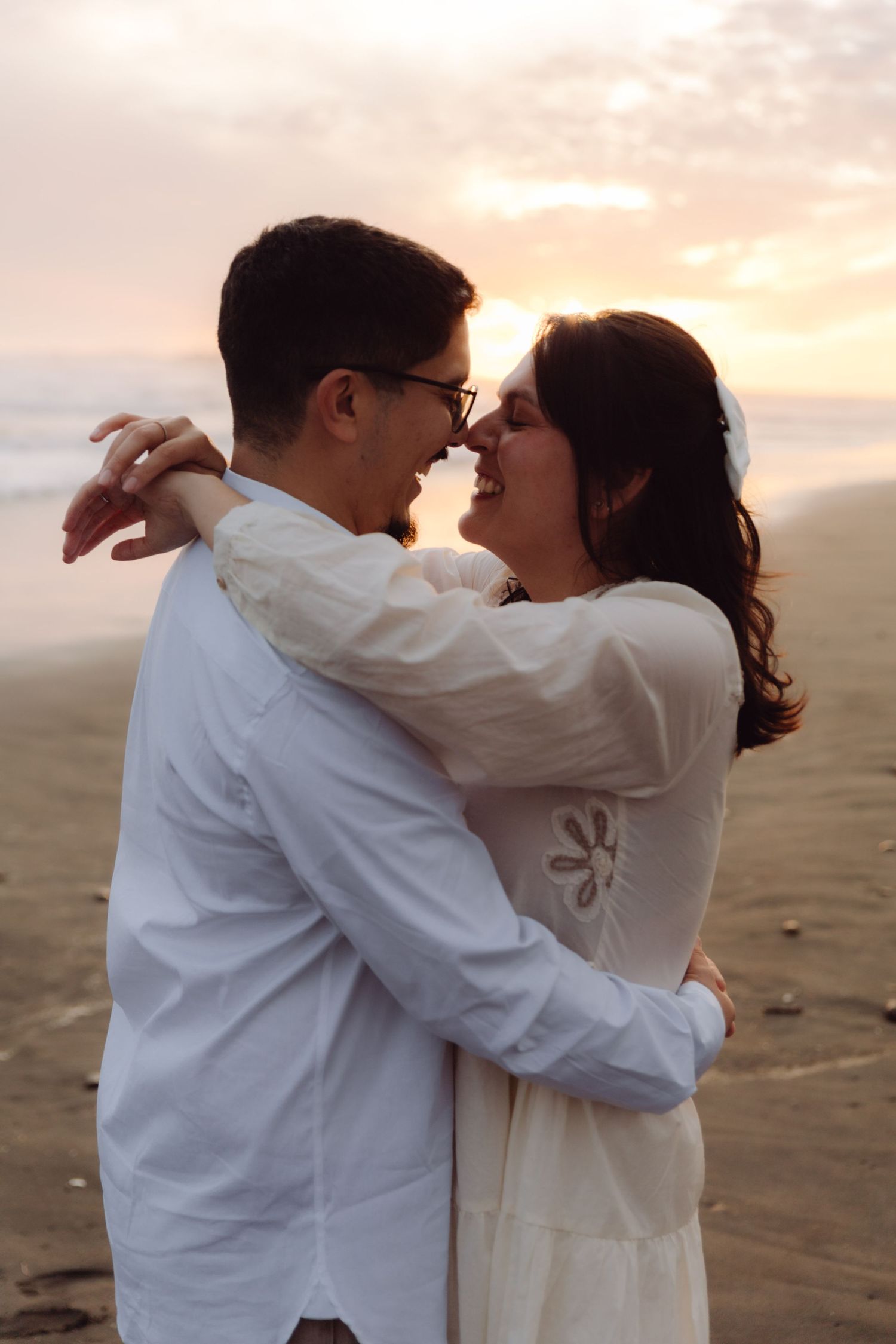 Couple sharing a tender nose-to-nose moment while embracing on a beach at golden hour sunset.
