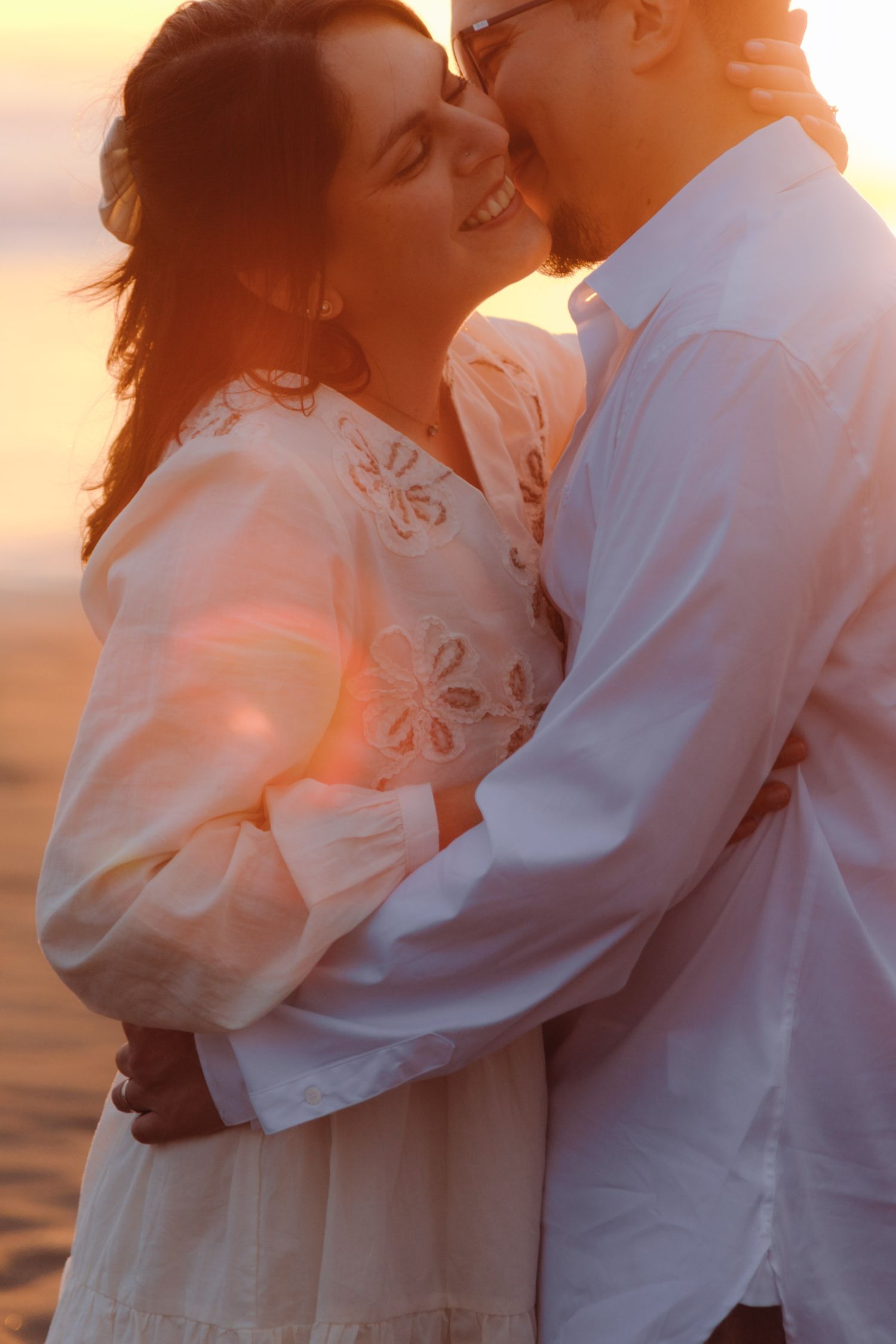 Close up of couple embracing with warm sunset lens flare on romantic beach photoshoot.