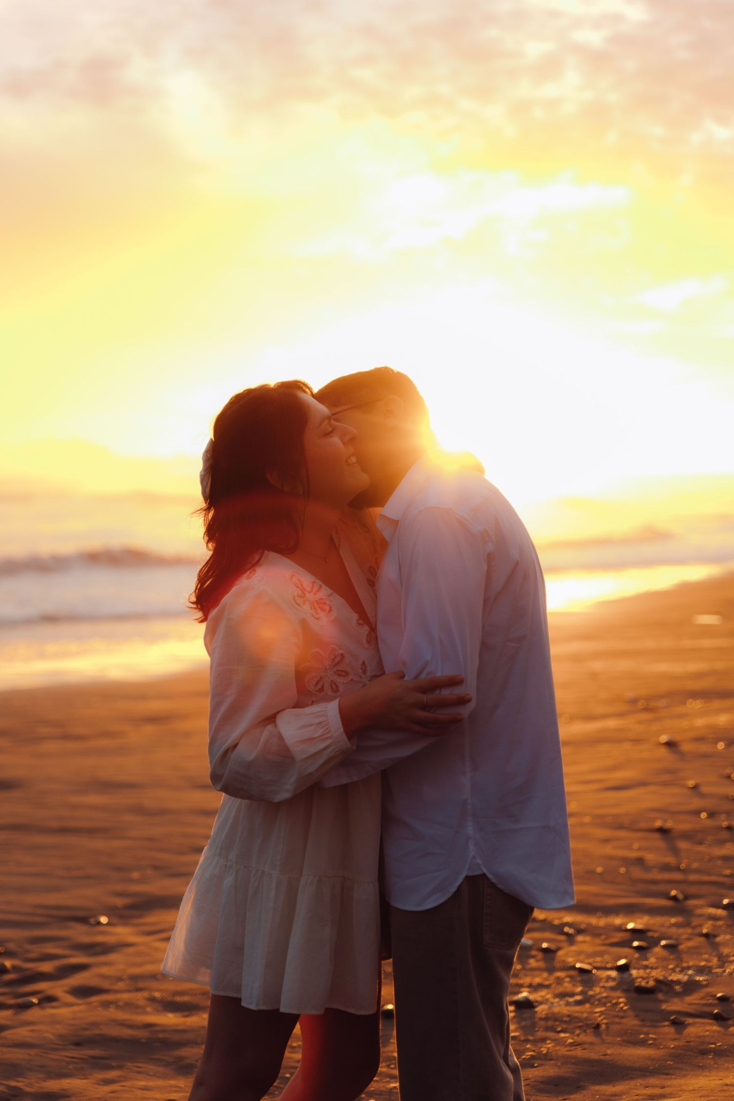 Couple sharing a kiss silhouetted against vivid golden sunset on sandy beach.