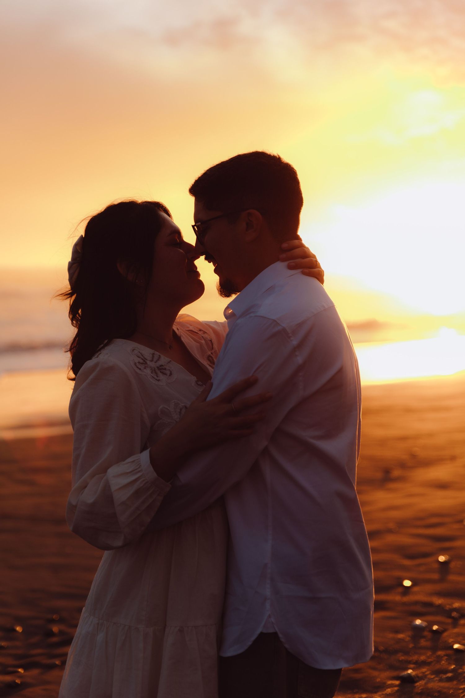 Romantic couple embracing on beach at golden sunset, faces close together in tender moment.