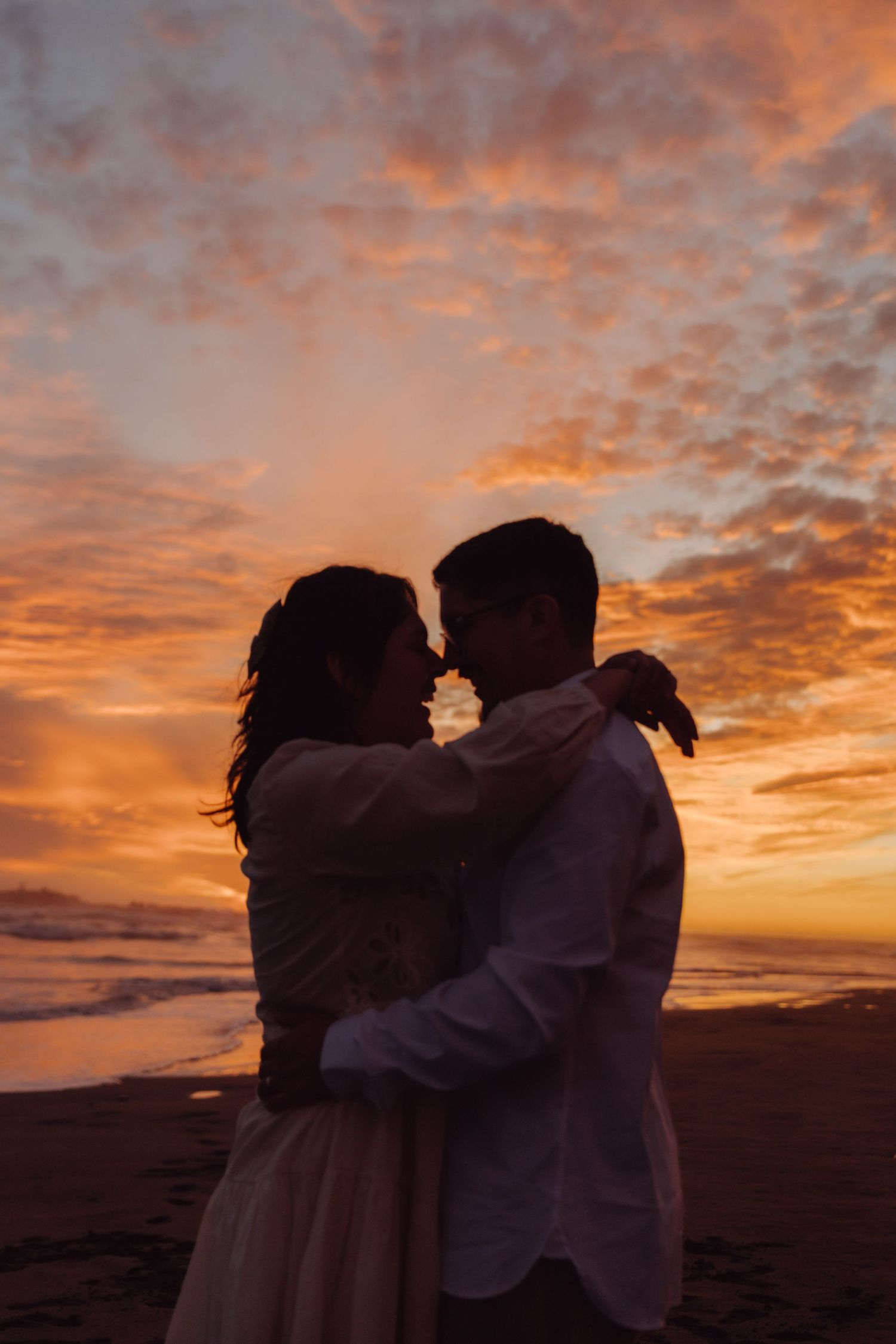 Romantic couple silhouette embracing on beach at stunning orange sunset.