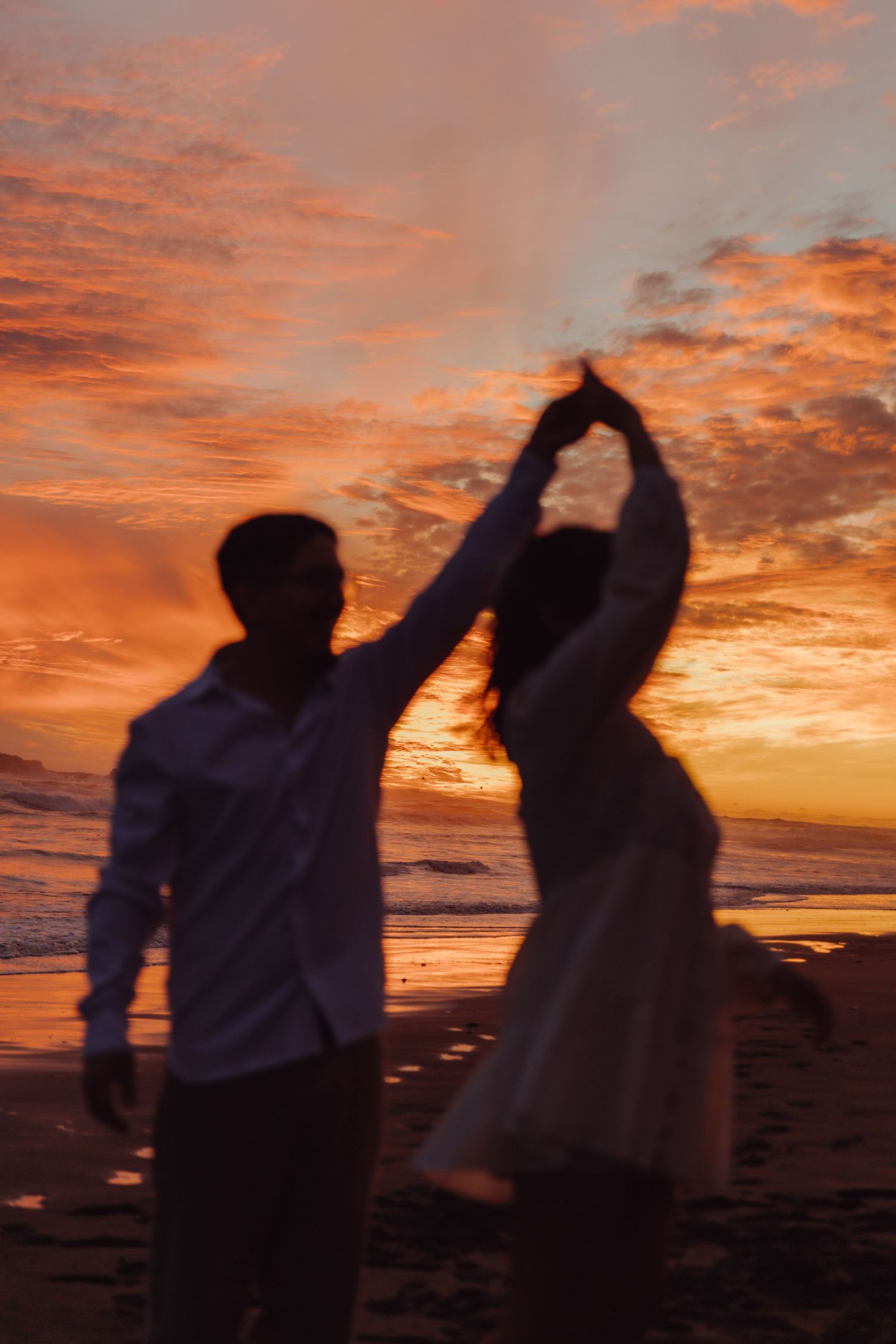 Blurred silhouette of couple dancing on beach during breathtaking orange sunset.