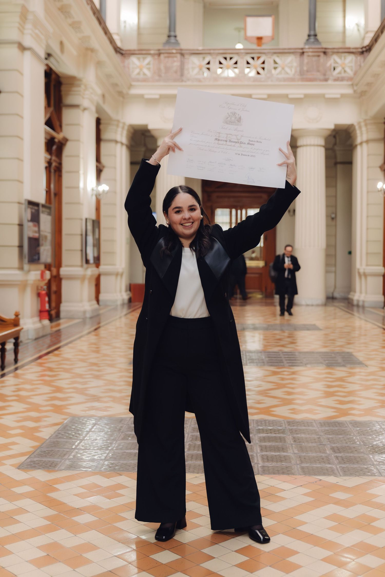 Joyful graduate raises diploma overhead in grand columned ceremonial hall.
