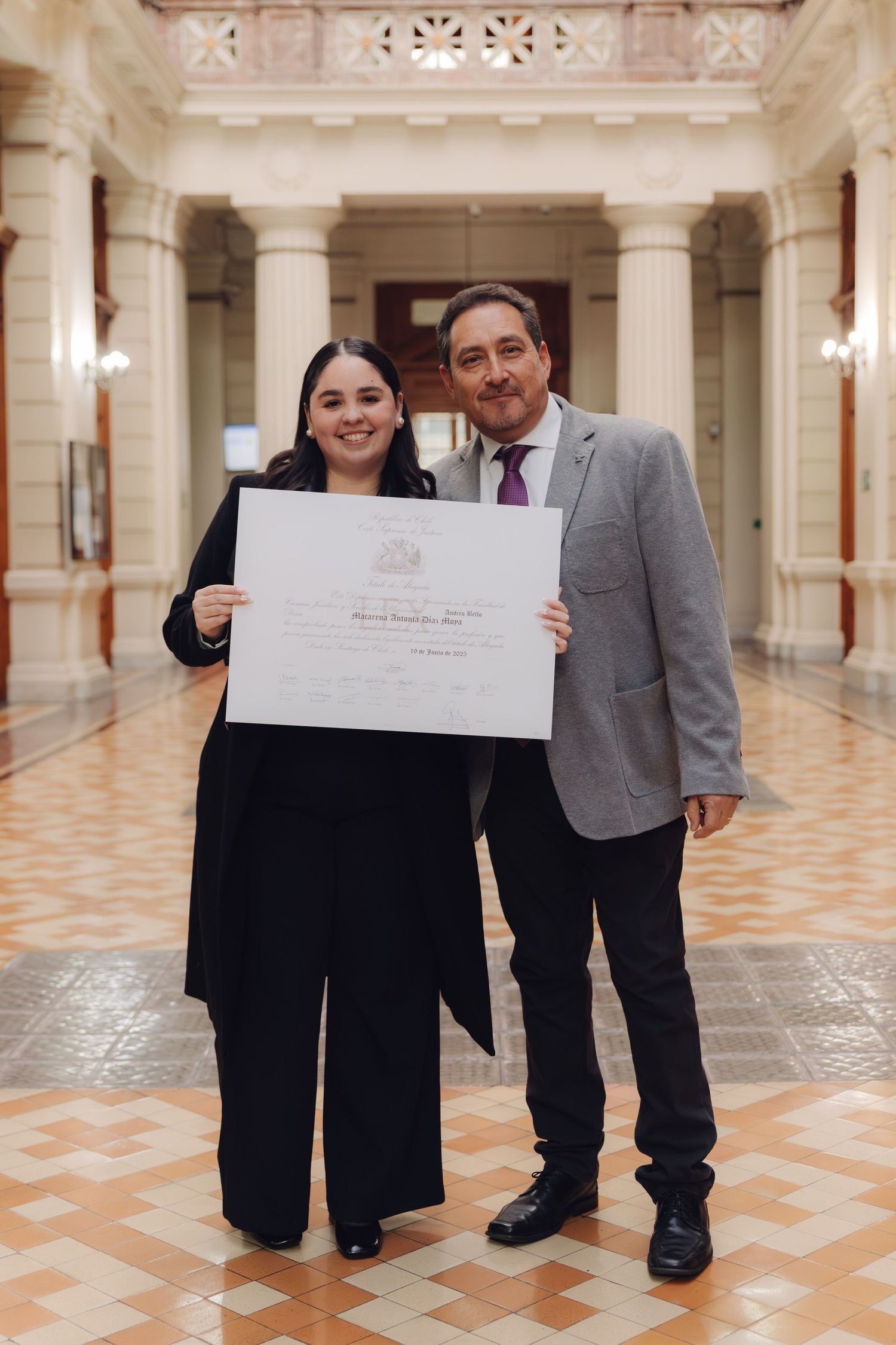 Female graduate and suited man proudly display diploma in elegant hall.