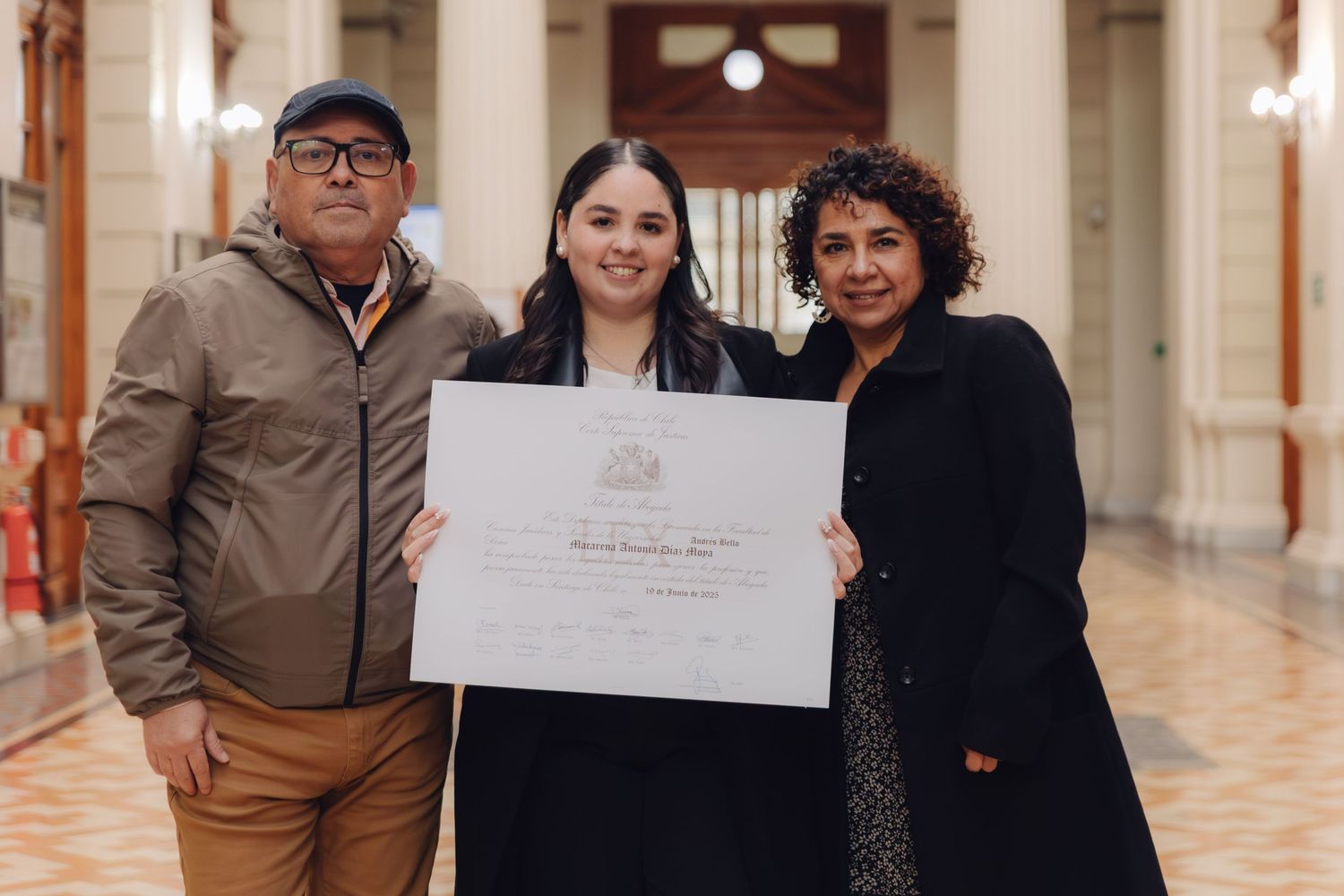 Graduate celebrates milestone with two family members holding diploma indoors.