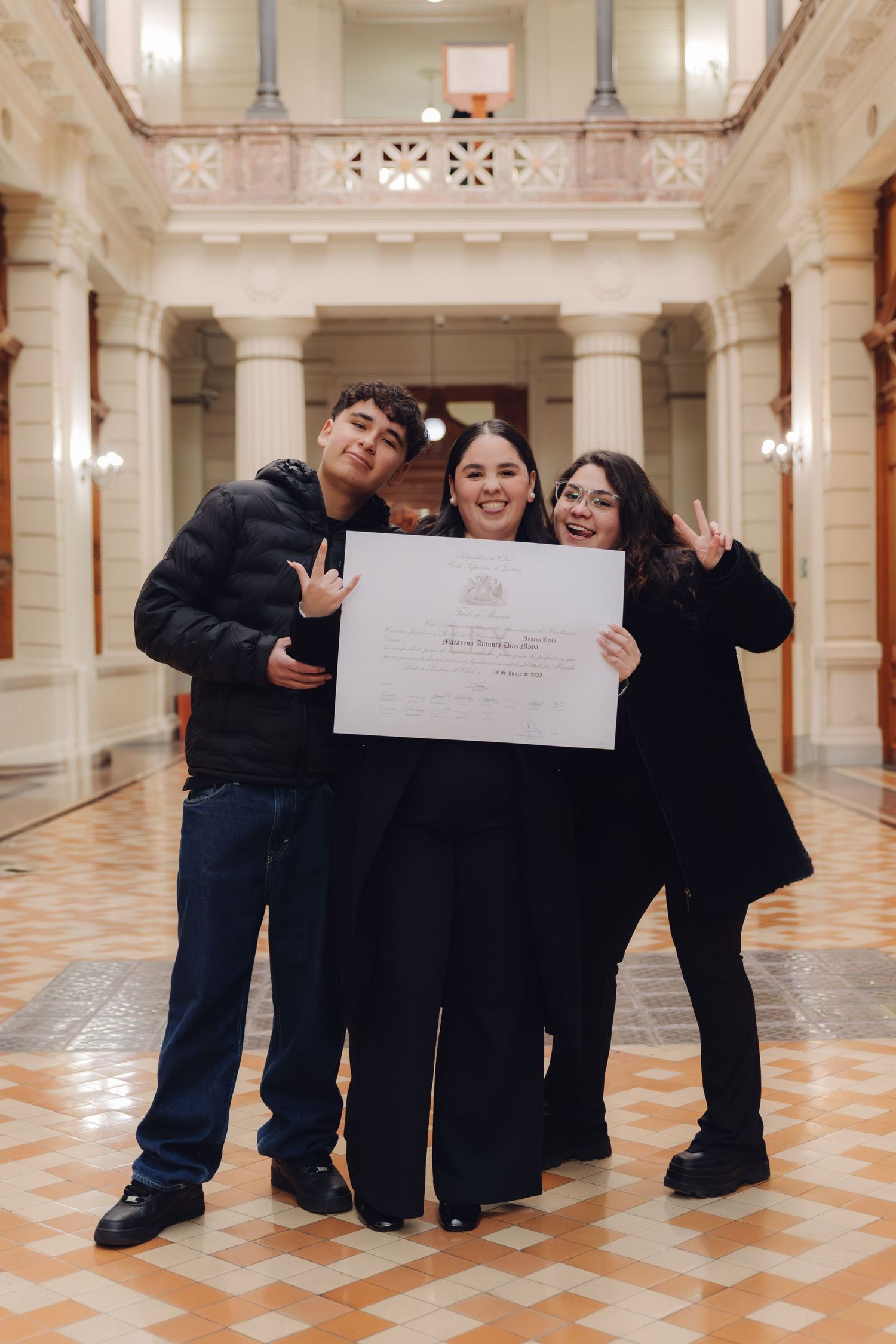 Three young people celebrating a graduation milestone while holding a diploma certificate in an elegant building.