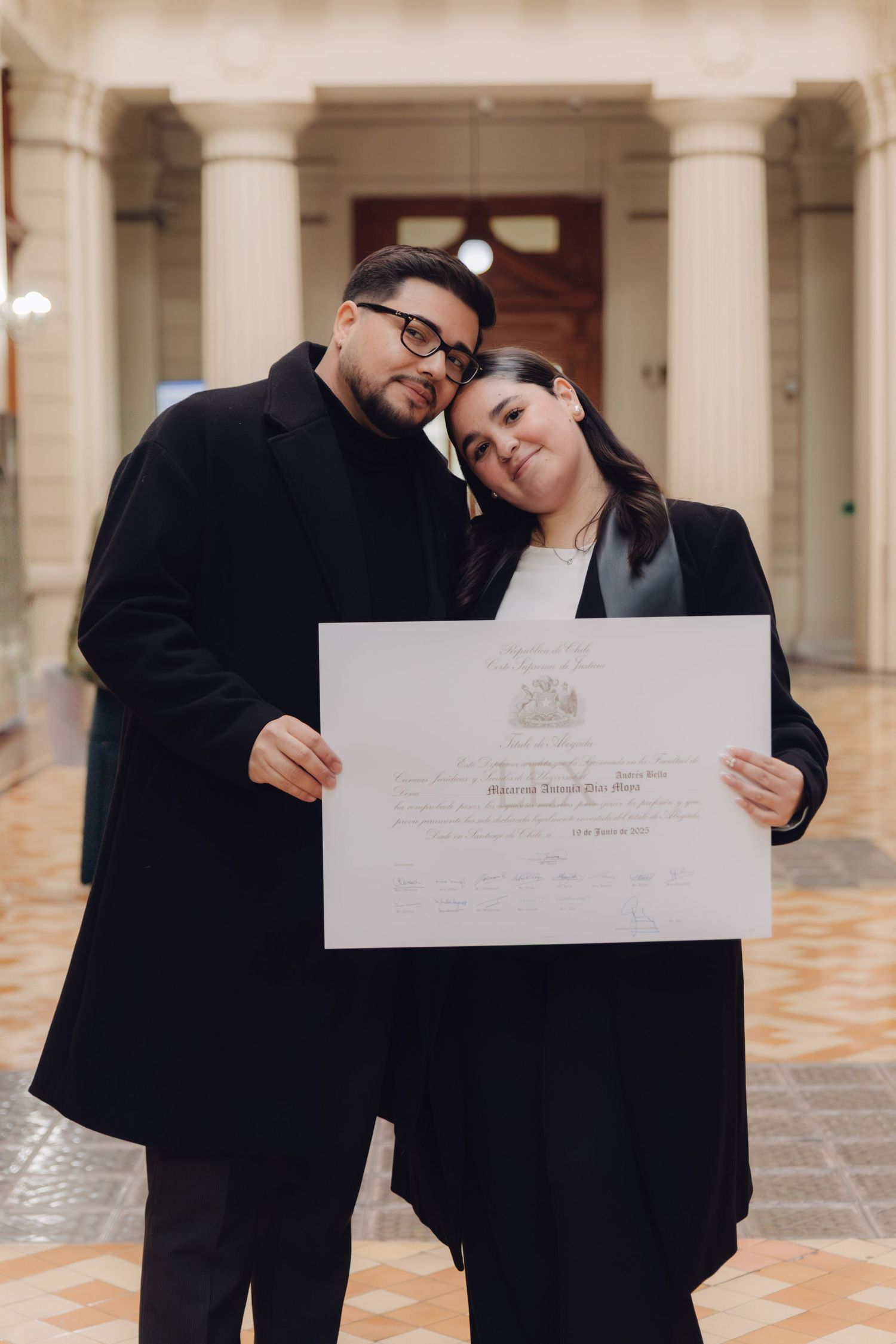 Couple proudly displaying a graduation diploma certificate together in a grand columned hallway.