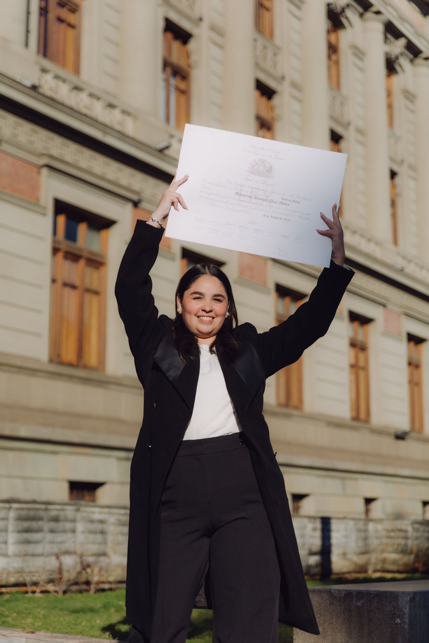 Joyful graduate raising her diploma certificate above her head outside a classic university building.