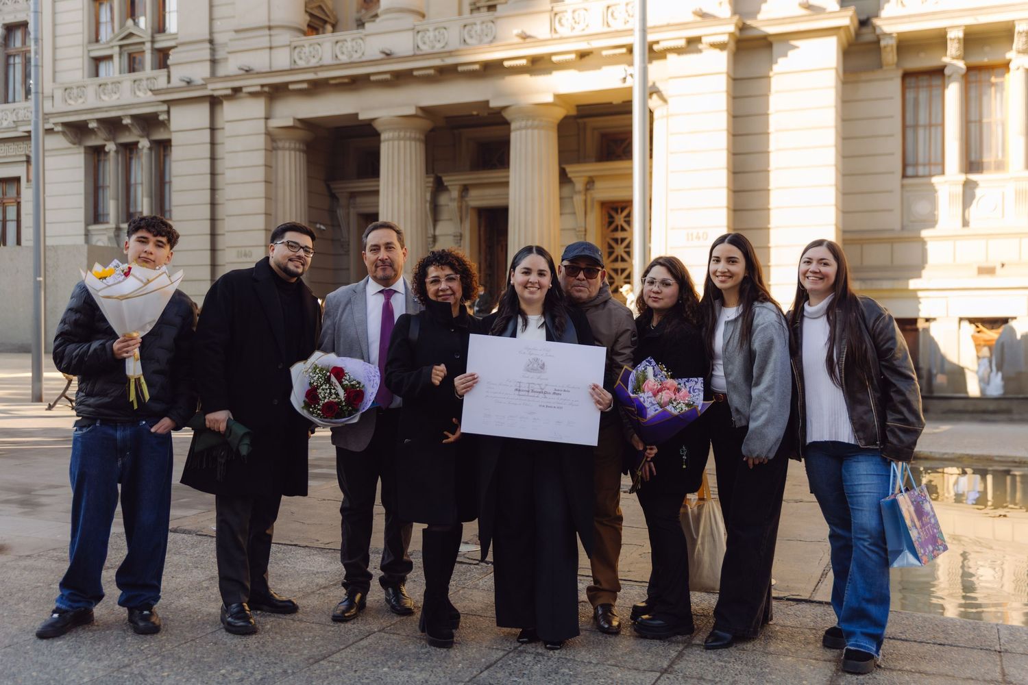 Graduate holding diploma certificate celebrating with group of family and friends outside grand building.