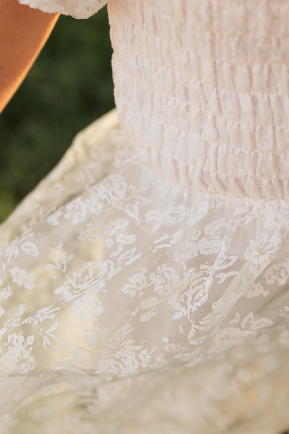 Close-up detail of white floral lace fabric on elegant smocked dress outdoors.
