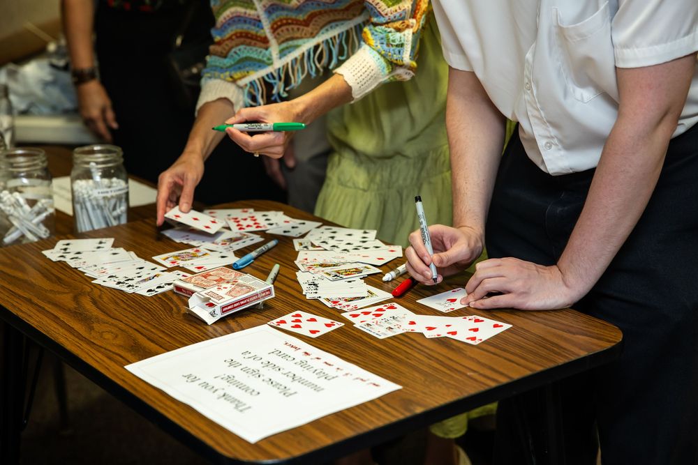 People sorting and writing on playing cards spread across a wooden table during a card game activity.