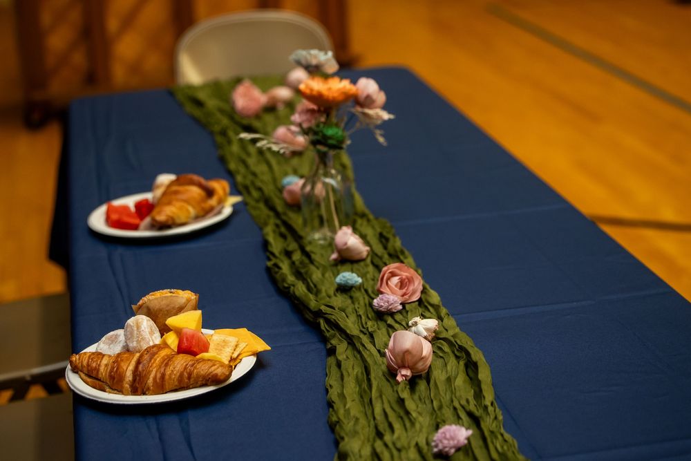 Elegant table with blue cloth, floral centerpiece, and plates of croissants and fruit in a decorated hall.