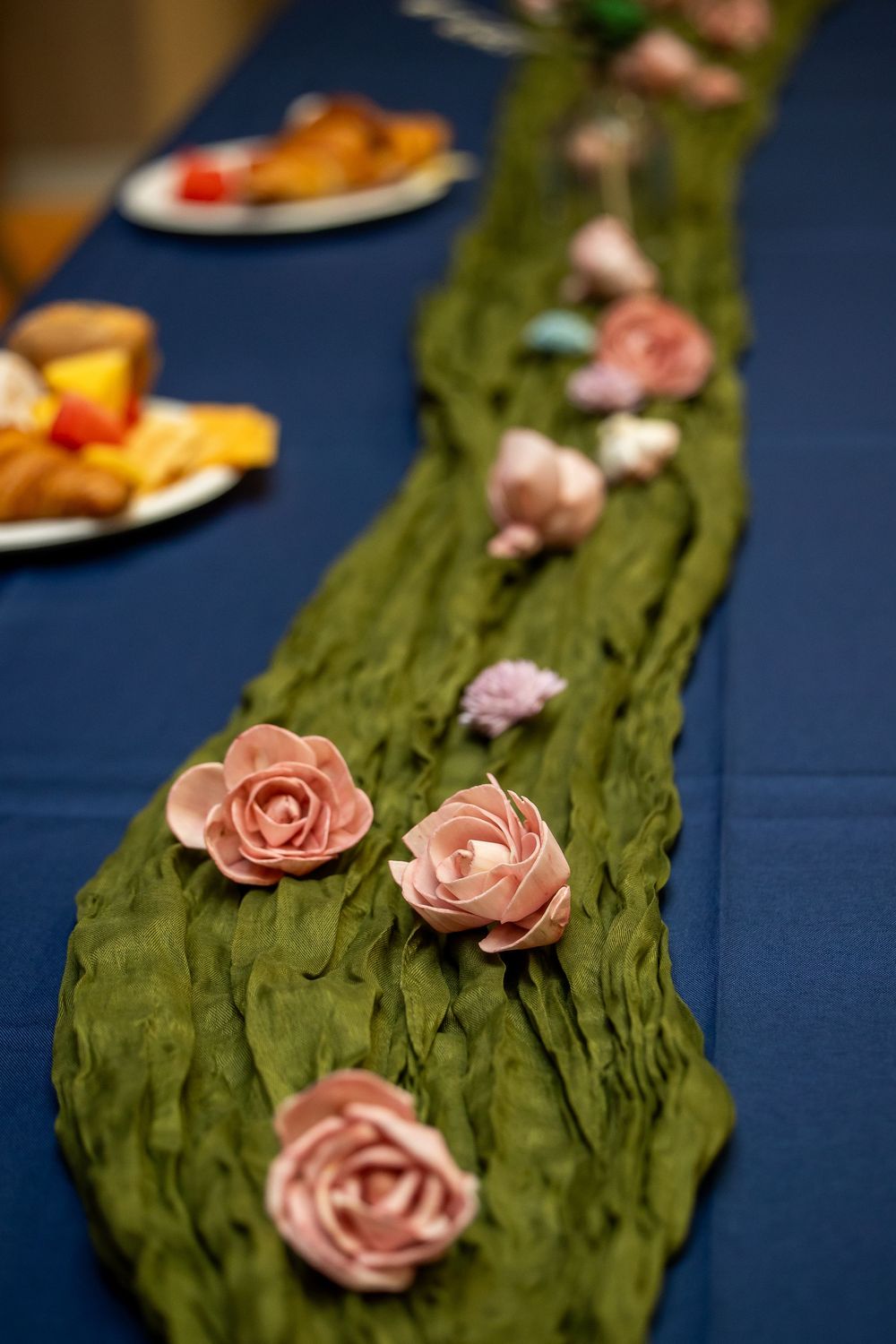 Green textured table runner adorned with pink roses on a blue tablecloth at an elegant event.