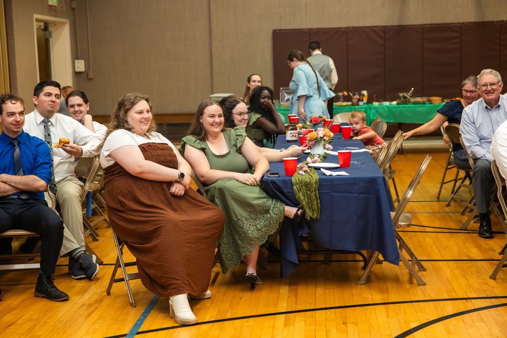 Group of people smiling and seated at tables during an indoor banquet event in a gymnasium.