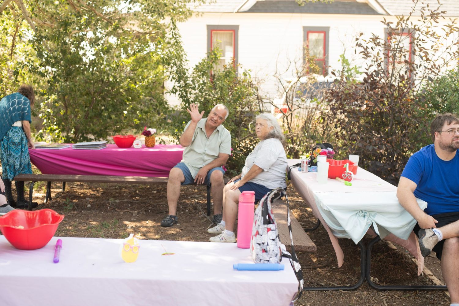Elderly people gathered outdoors at a backyard party with tables, food, and drinks on a sunny day.