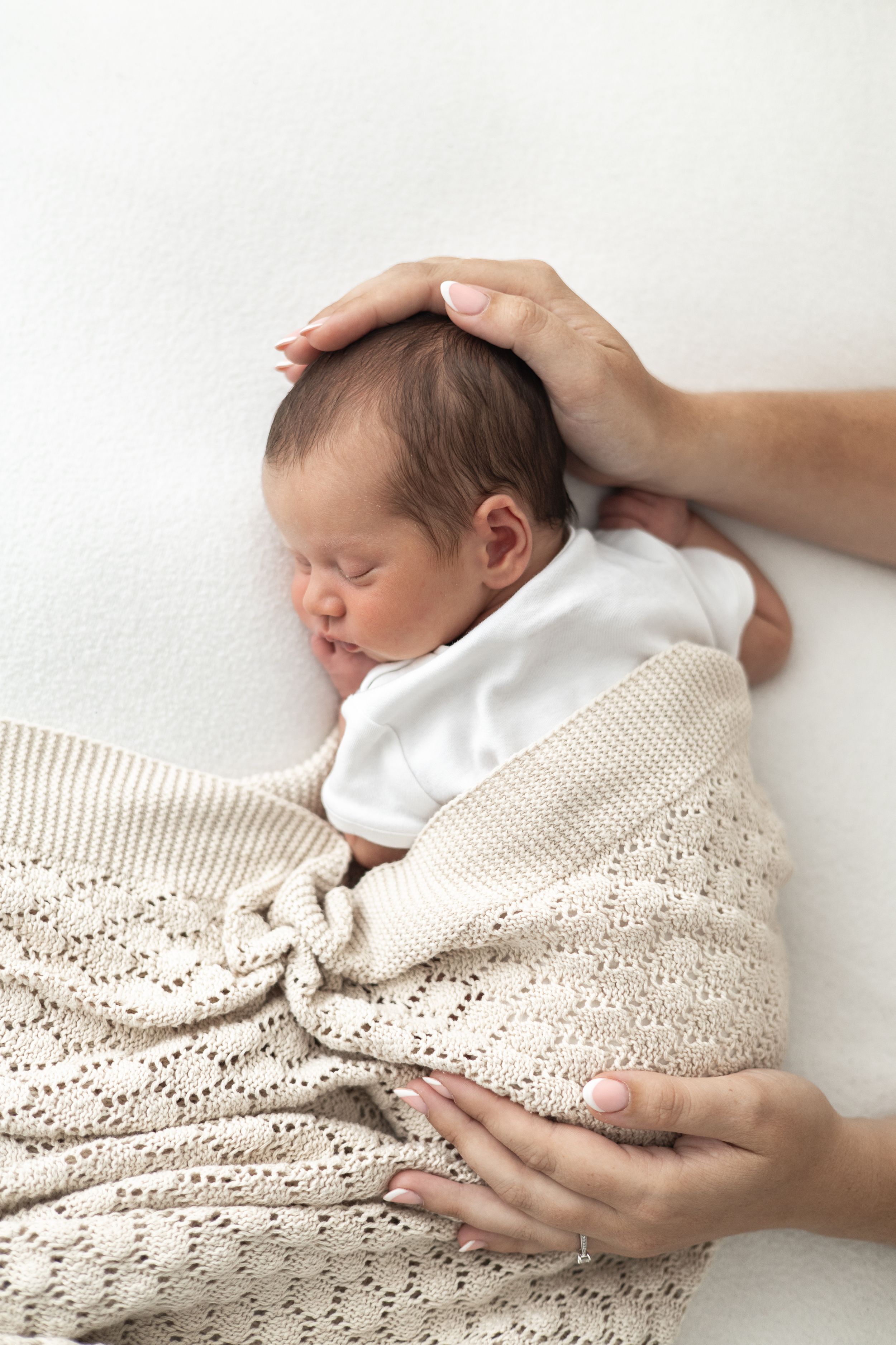 Newborn baby sleeping wrapped in a beige knit blanket while a mother gently cradles their head natural baby photography Nottingham