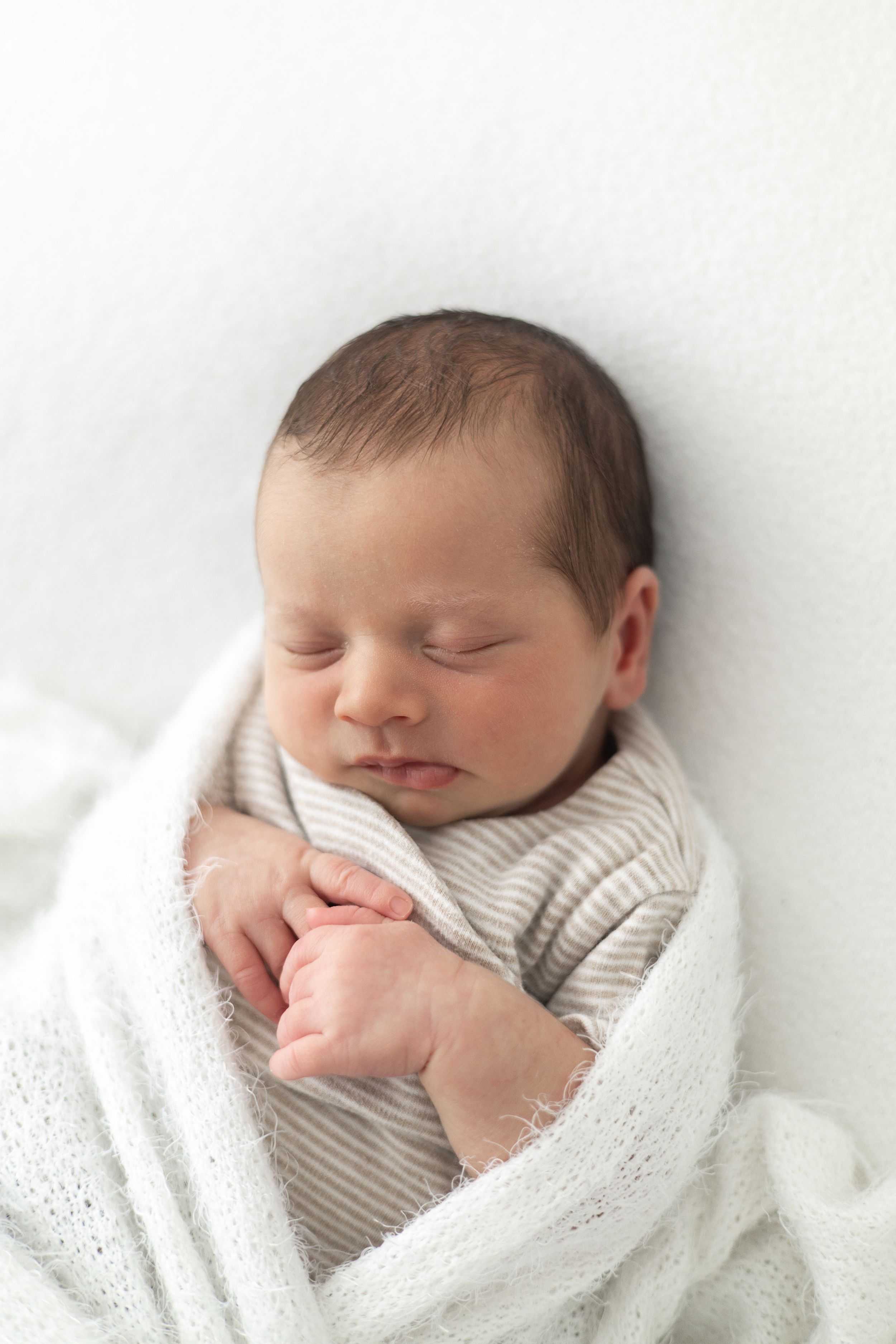 Peaceful newborn baby sleeping wrapped in a white knit blanket with tiny hands visible natural baby photography Nottingham
