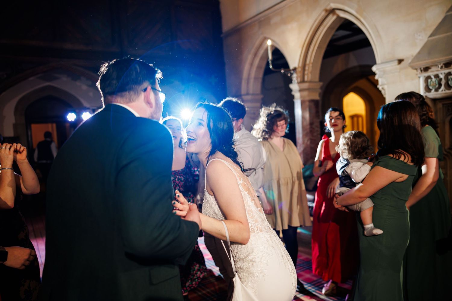 Bride and groom share first dance at elegant wedding reception with guests and blue lighting.
