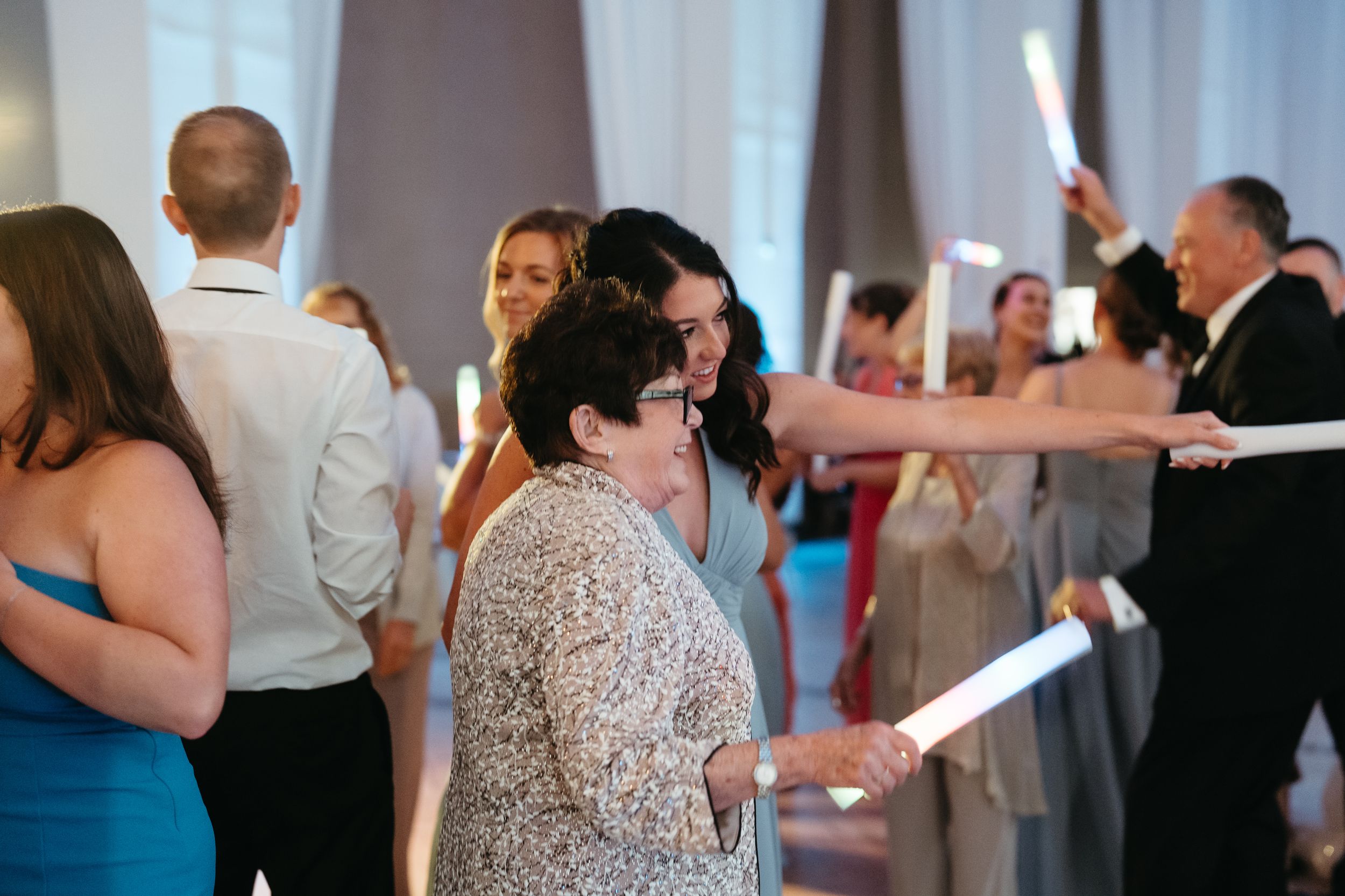 Guests celebrate at a wedding reception holding glowing light sticks on the dance floor.