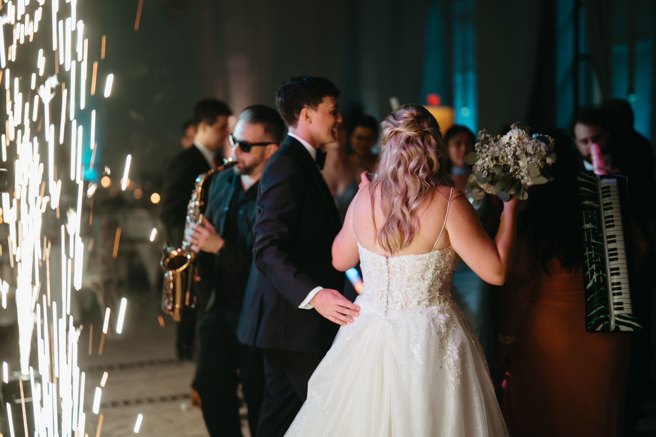 Bride and groom walk through reception hall with live saxophone and accordion band performing at elegant wedding.