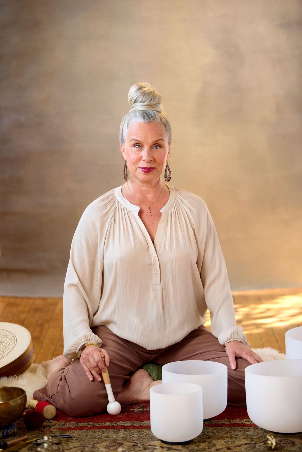 Woman meditating with crystal singing bowls and mallet in a serene studio setting for sound healing therapy.