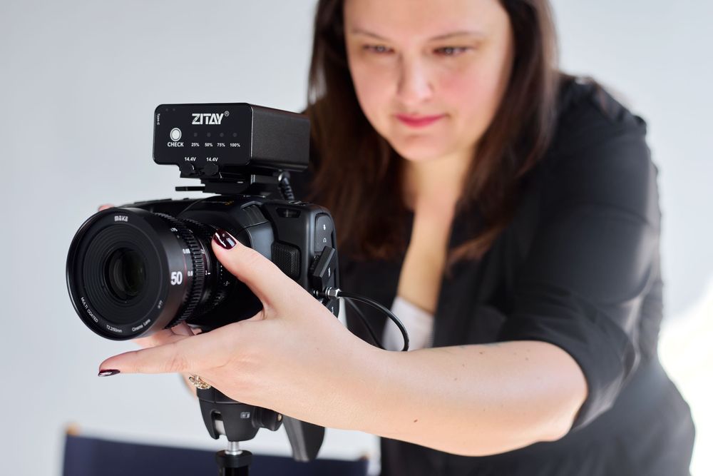 Woman photographer adjusting a professional DSLR camera with Zhiyun accessory mounted on top in a studio.