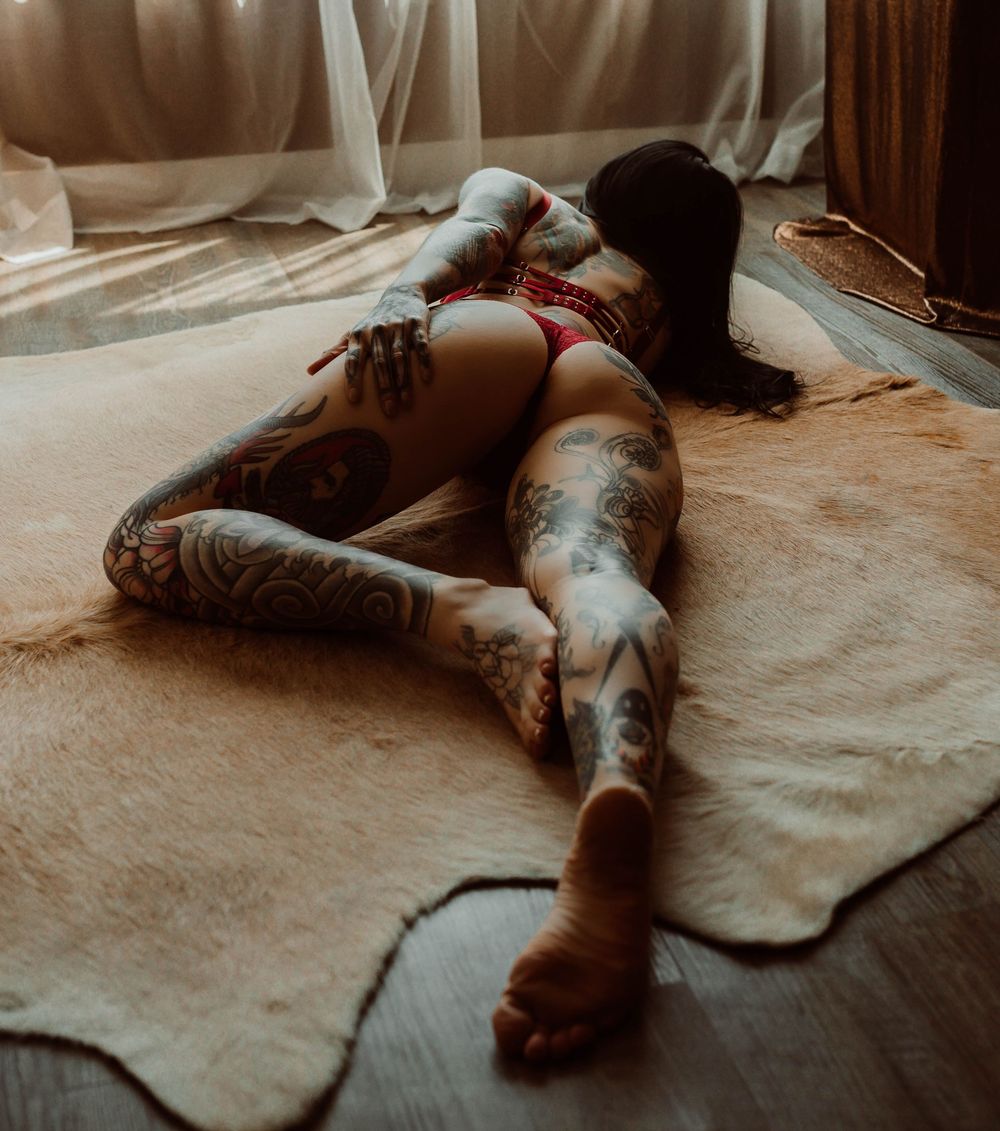 Heavily tattooed woman lying on a fur rug in red lingerie with a Wisconsin boudoir photographer.