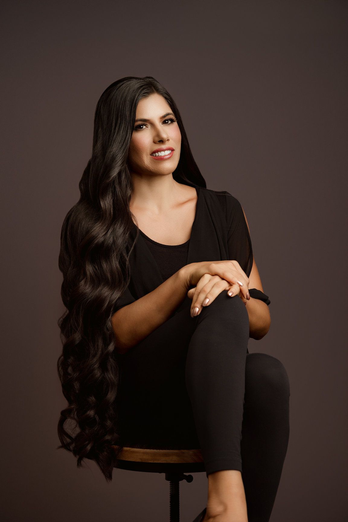 Miami mini headshot portrait of a seated woman in black against a warm brown studio background.