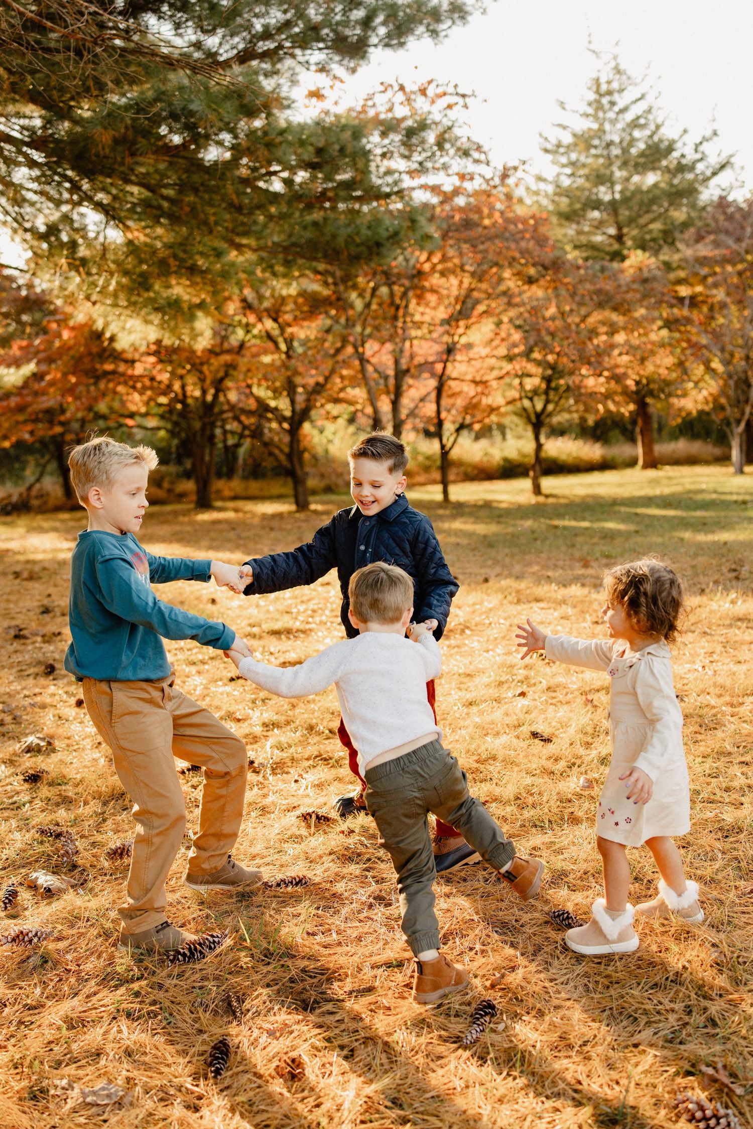 Four children playing ring-around-the-rosy in an autumn park with colorful fall foliage in the background.