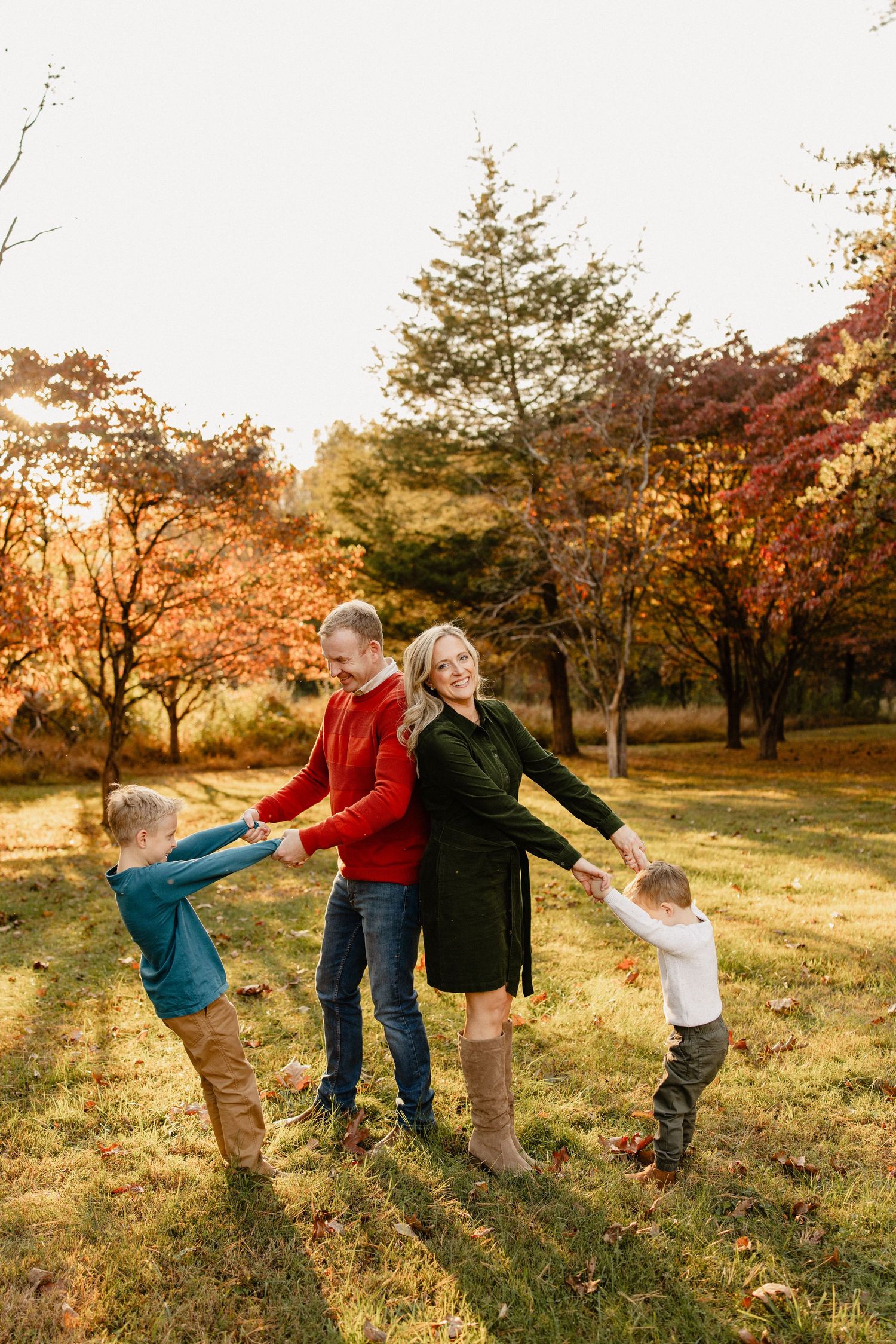 Family of four playing outdoors in autumn park with colorful fall foliage trees in background.