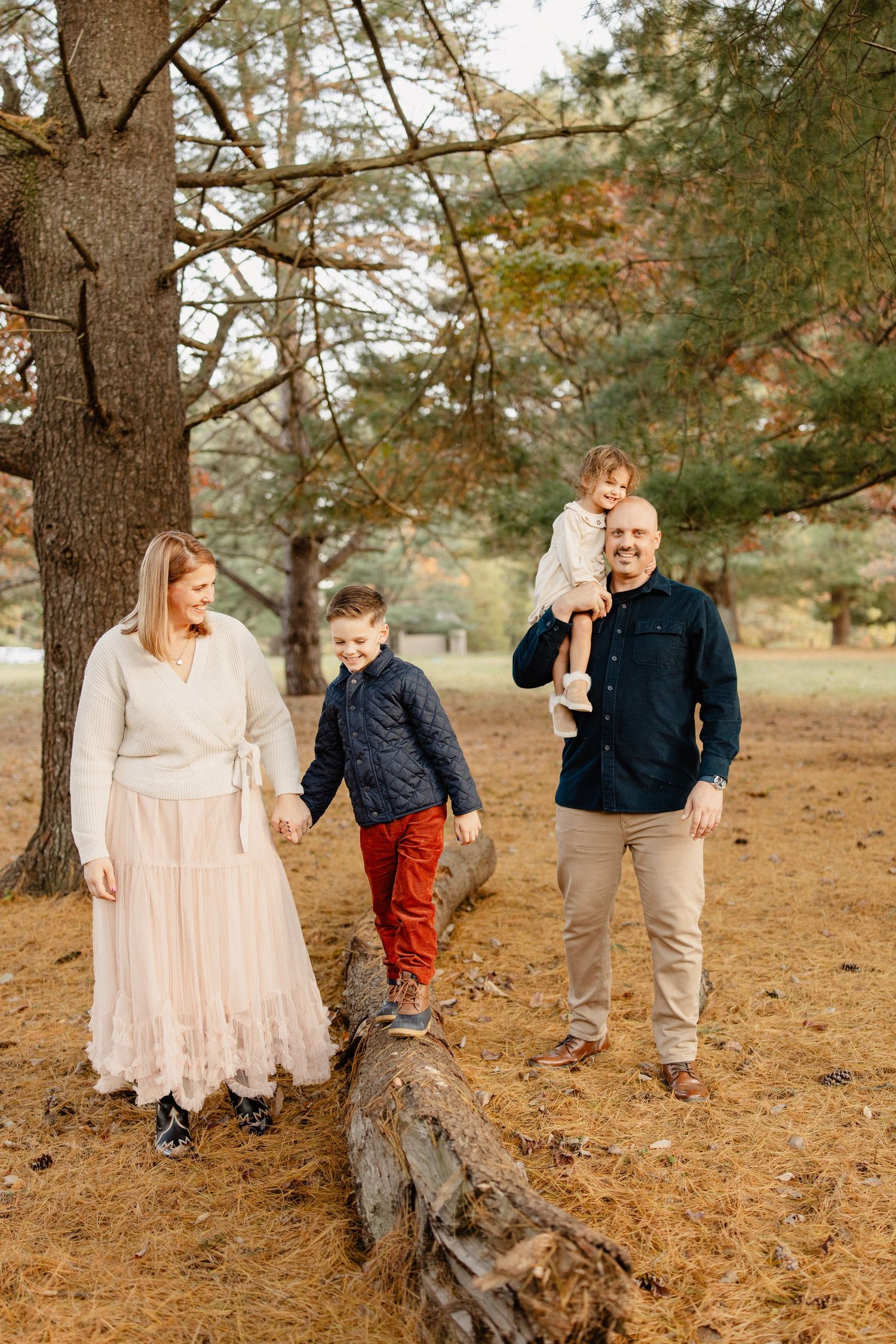 Family of four enjoying an autumn walk in the park, with two boys and parents dressed in fall colors among pine trees.