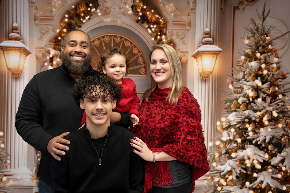 Joyful family of four poses together in festive red and black outfits near Christmas tree.