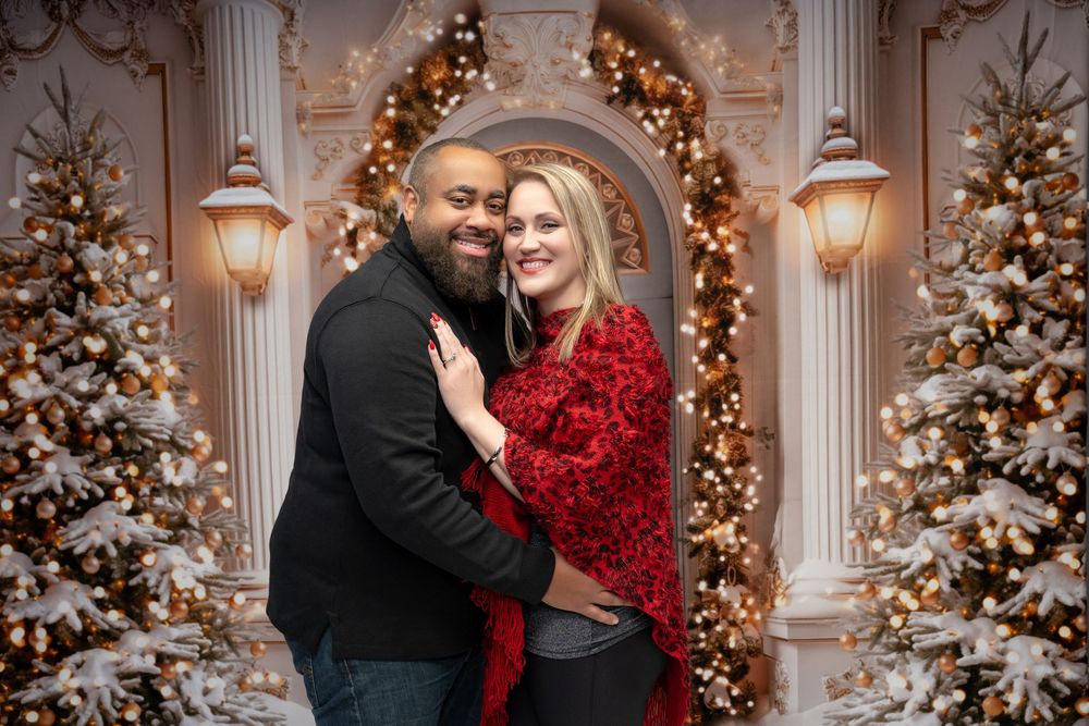 Couple embracing in front of festive Christmas trees with warm lights in elegant holiday portrait.