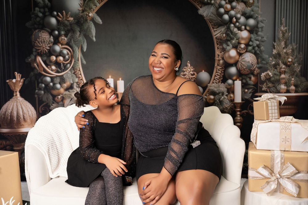 Mother and daughter in black outfits laughing together on white sofa with holiday decor.