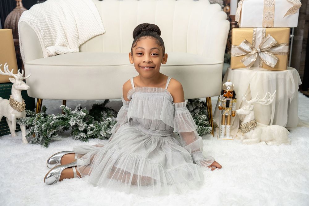 Young girl in silver tulle dress sitting on snowy floor with holiday decorations.