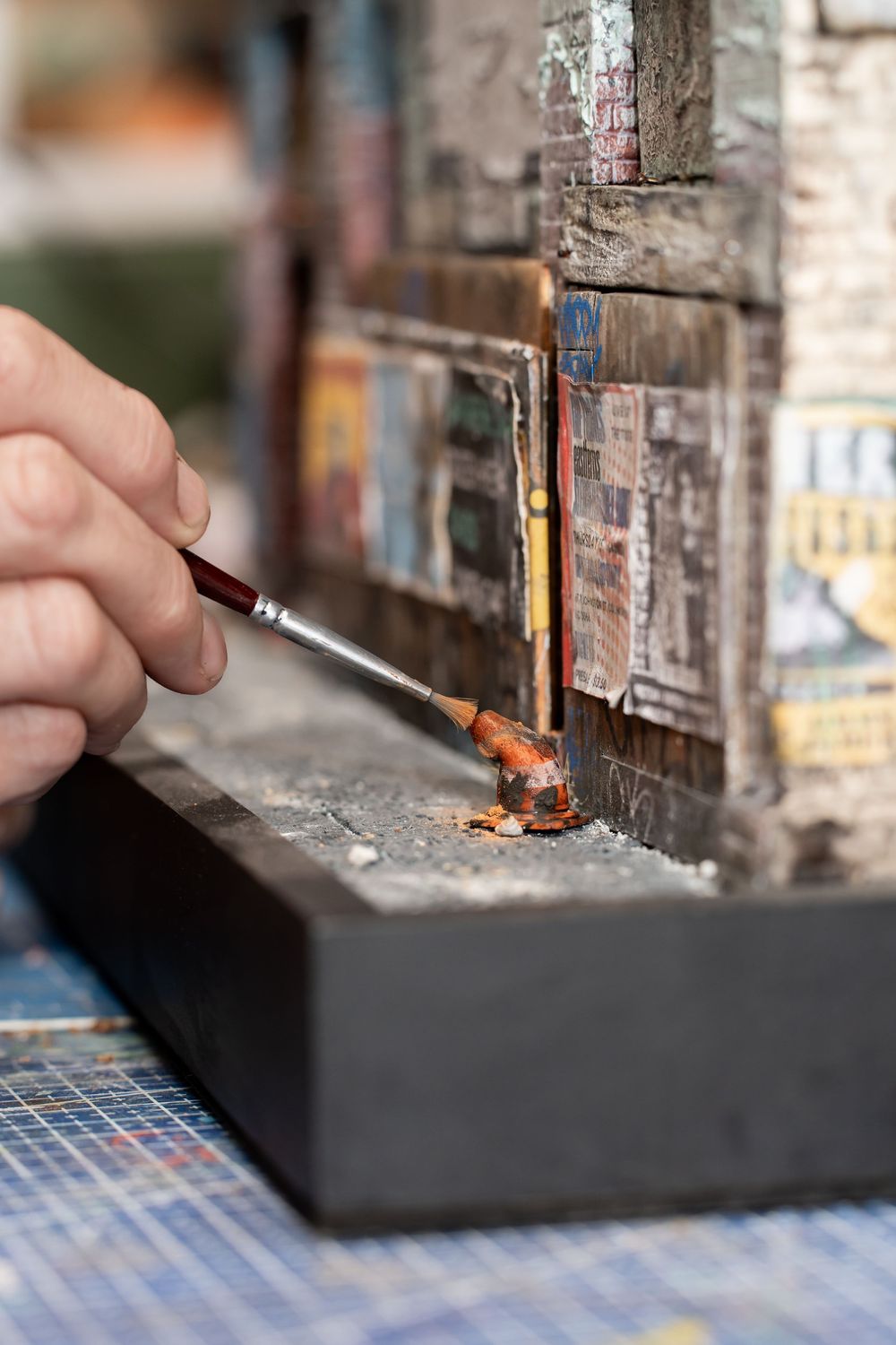 A hand carefully painting details on a miniature building model with a fine brush, showcasing intricate diorama craftsmanship.