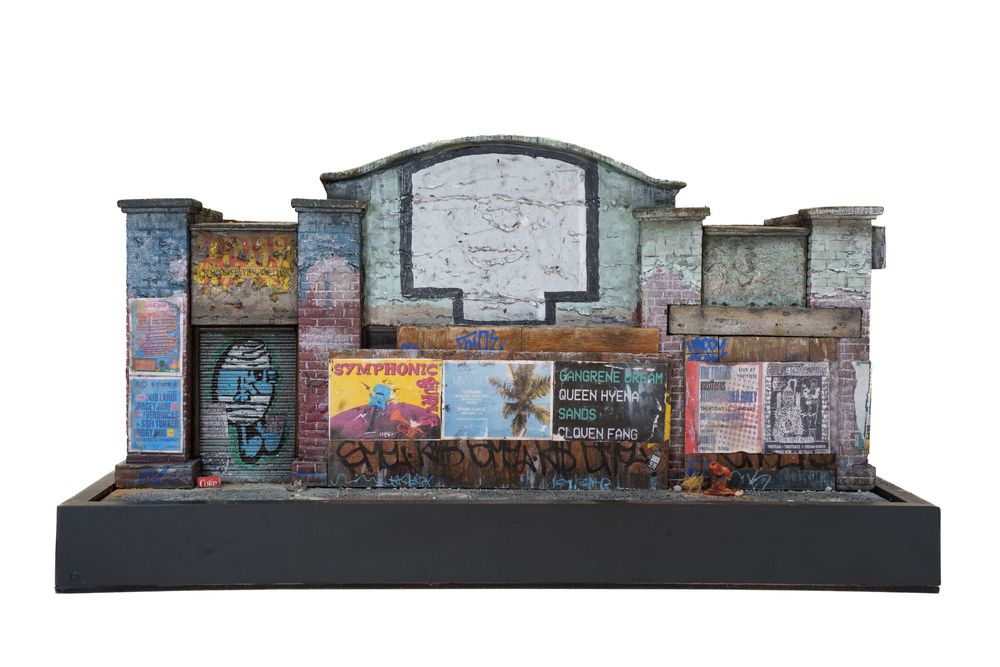 Detailed scale model diorama of a graffiti-covered urban building facade with arched entrance on black base.