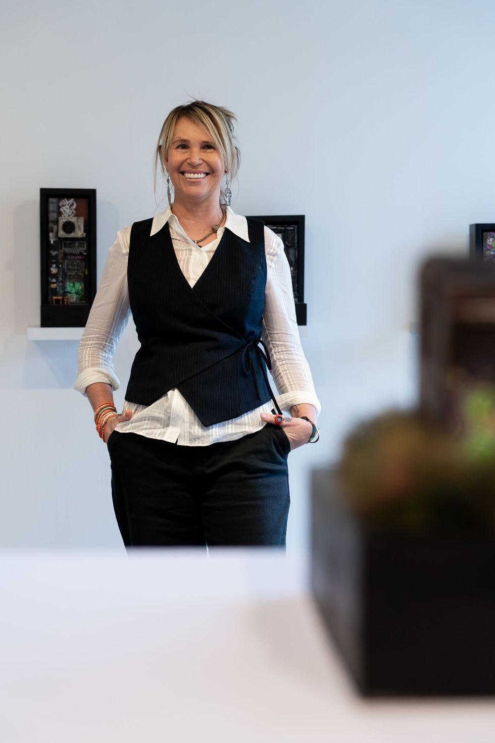 Smiling woman in black vest and white shirt standing confidently in a modern gallery space.