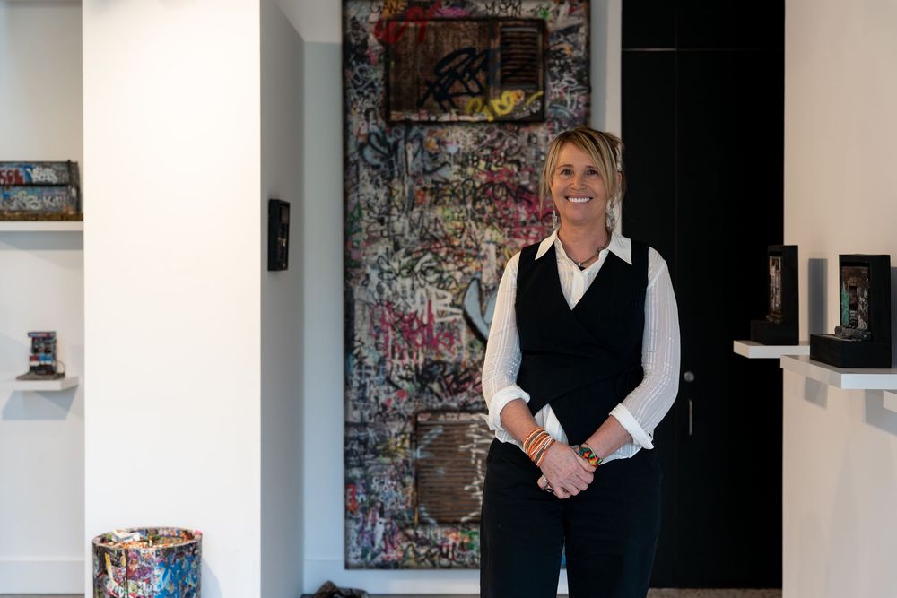 Woman smiling in art gallery wearing black vest and white shirt, surrounded by colorful artwork and sculptures.