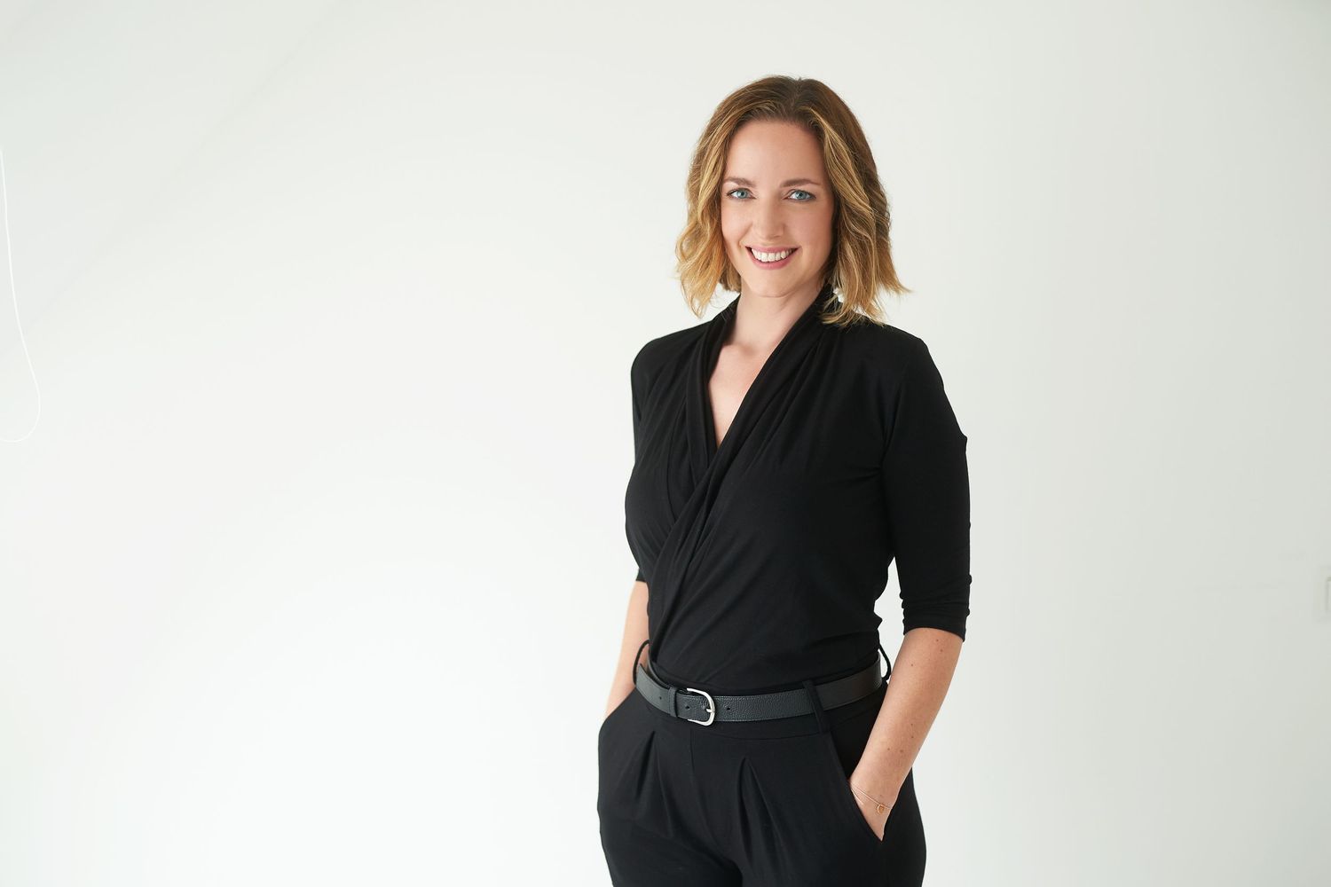Business Portrait Wien - Geschäftsfrau in schwarzem Outfit, die selbstbewusst vor weißem Hintergrund lächelt, modernes Geschäftsporträt.