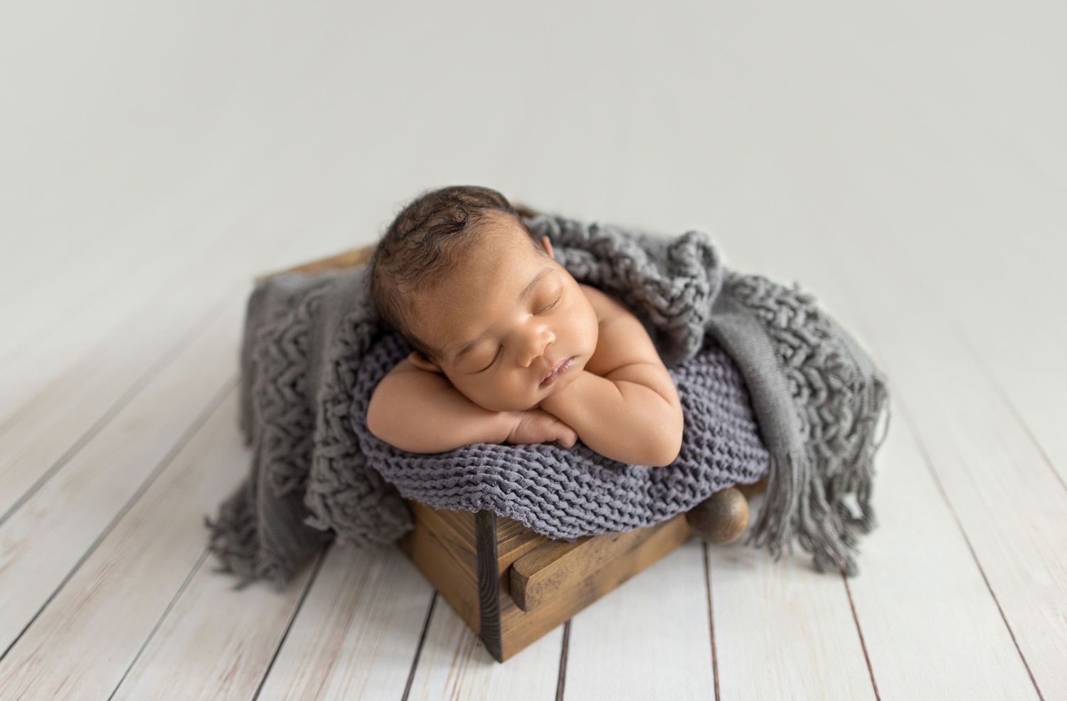 Newborn baby sleeping peacefully in sage green wrap and hat on matching green backdrop.