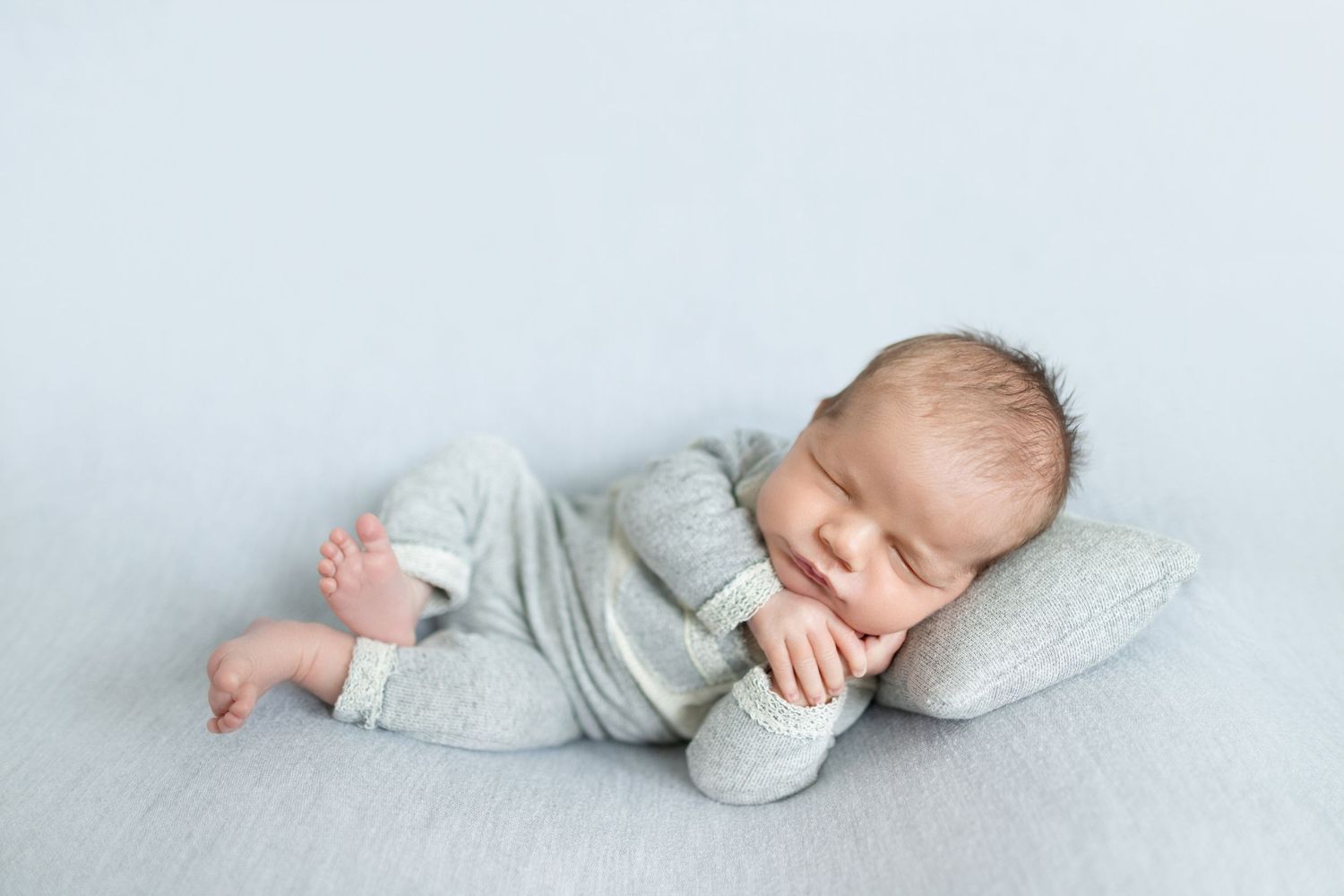 Peaceful newborn baby sleeping in gray onesie on small pillow against soft light blue background.