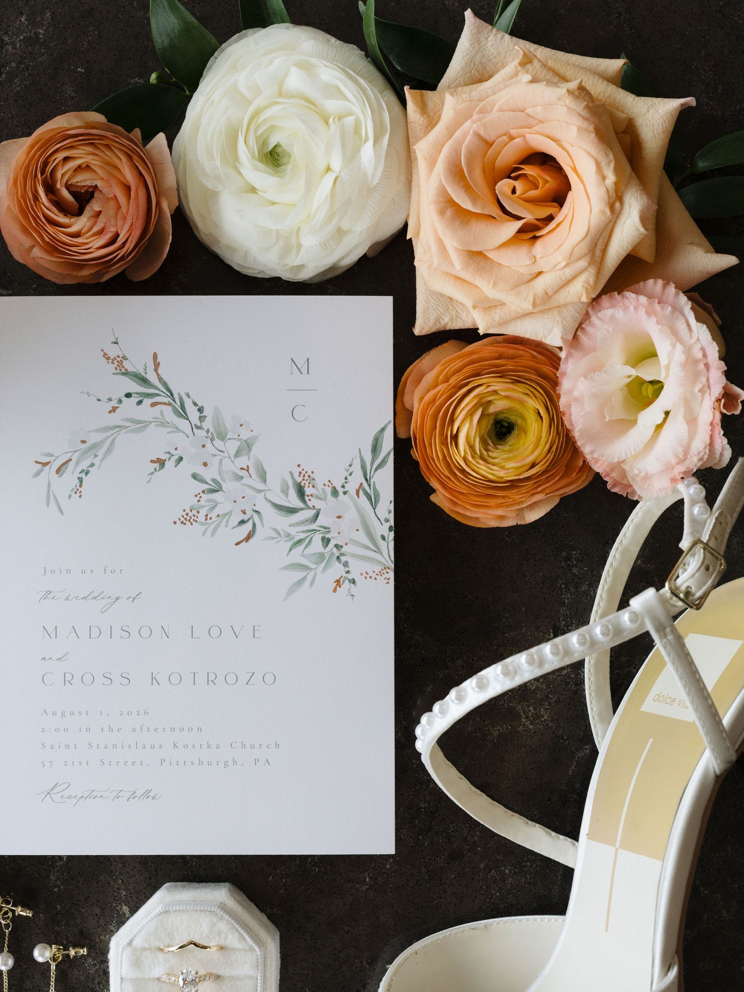 Wedding flat lay with a floral invitation for Madison Love and Cross Kotrozo, peach roses, ranunculus, pearl bridal heels and a ring box.