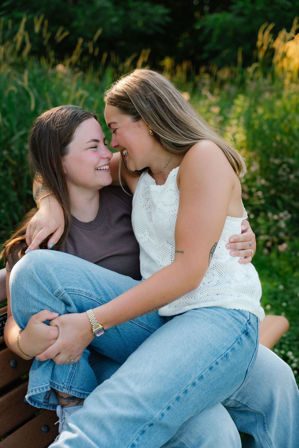 Two young women share a tender moment on a park bench, smiling and embracing outdoors.