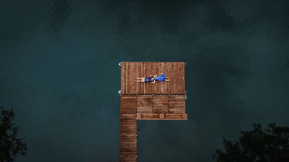A drone flies over a wooden platform structure against a dark stormy sky with trees visible below.