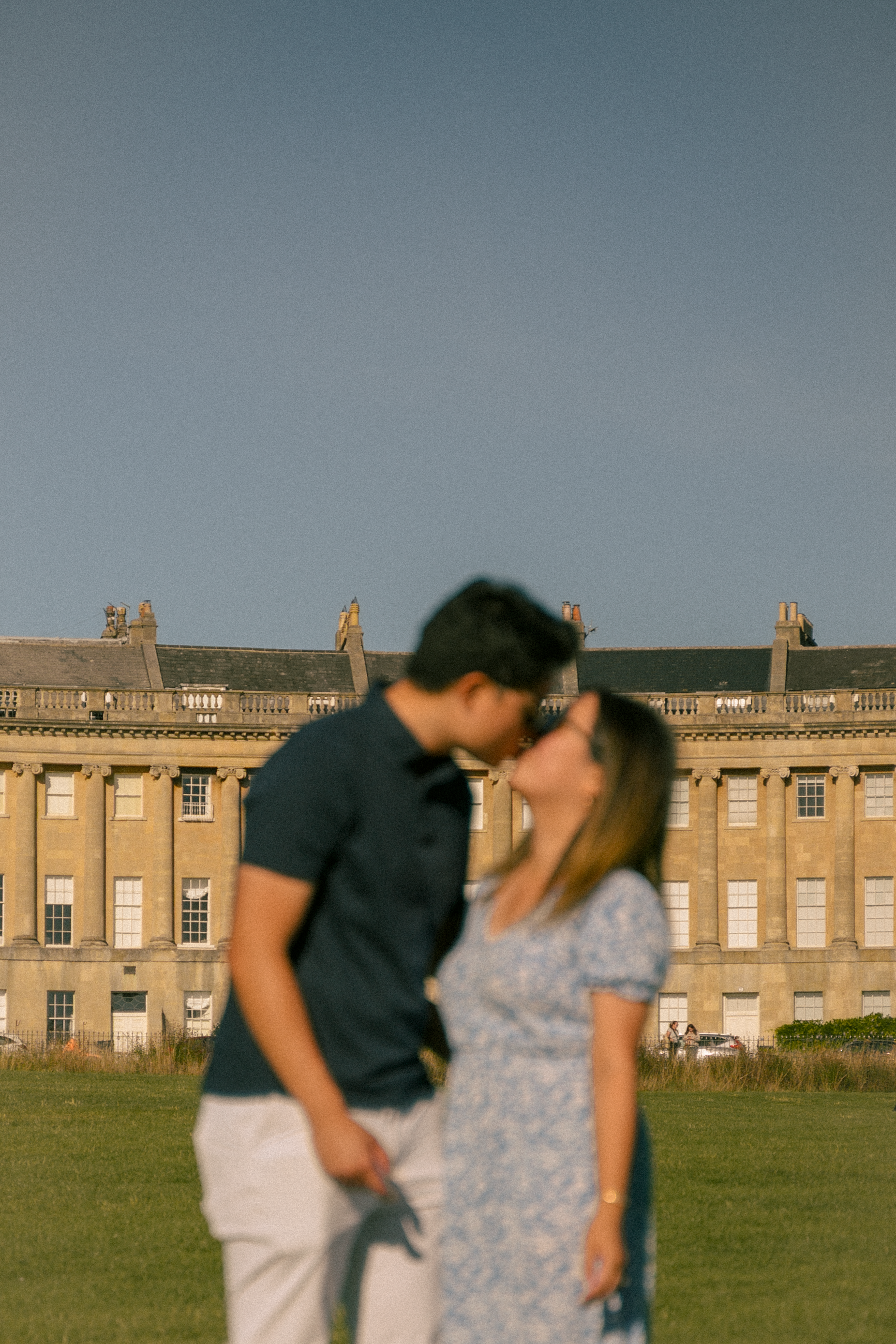 Couple sharing a romantic kiss in front of the Royal Crescent in Bath, England, on a sunny day.