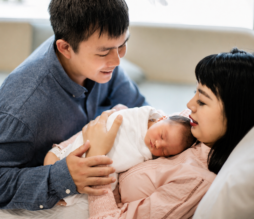 New parents lovingly gaze at their newborn baby in a bright hospital room.